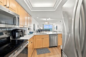 A modern kitchen with stainless steel appliances, wooden cabinets, and a view to the outside.