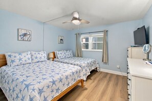 A bedroom with two beds, a ceiling fan, a window with curtains, and a TV on a cabinet. - Incredible Gulf View-Madeira Beach 3BD/2BA Beachfront Condo Rental (Madeira Beach)