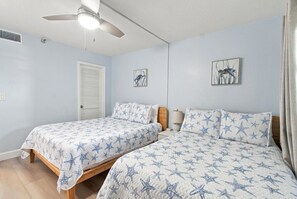 Un dormitorio con dos camas, un ventilador de techo y dos cuadros colgados en la pared.