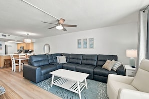 A modern living room with a sectional sofa, a coffee table, and a dining area with a kitchen in the background. - Seaview 302| Newly Remodeled Beachfront Condo with Expansive Gulf Views (Madeira Beach)