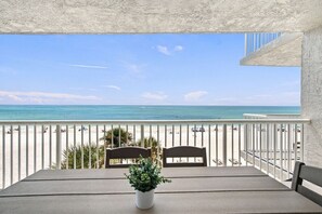A balcony with a view of the beach and ocean, a table with chairs, and a potted plant.
