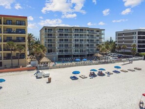A beachside hotel with multiple floors, a pool area, and several beach umbrellas. - Incredible Gulf View-Madeira Beach 3BD/2BA Beachfront Condo Rental (Madeira Beach)