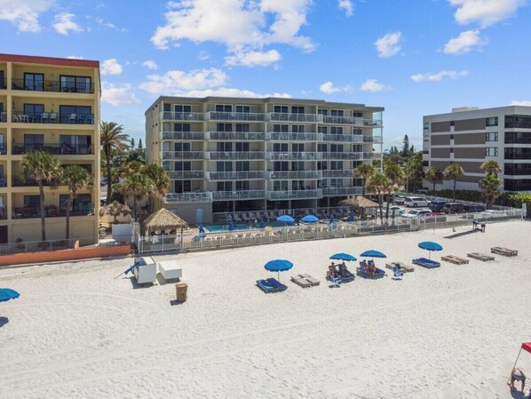 Hotel aan het strand met meerdere verdiepingen, een zwembadgedeelte en verschillende strandparasols.