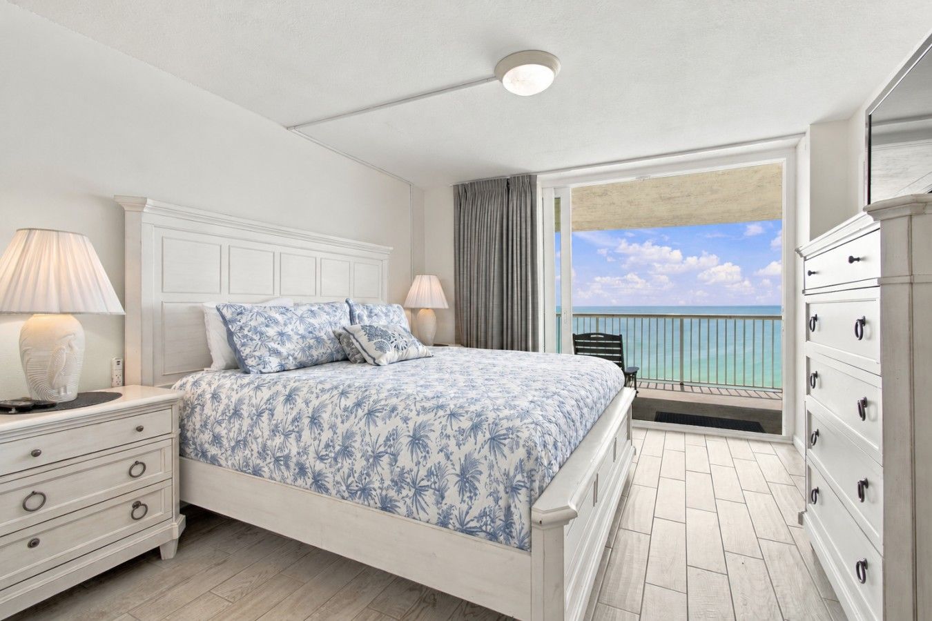 Ein Schlafzimmer mit Bett, Nachttischen, einem Schminktisch und einem Balkon mit Meerblick.