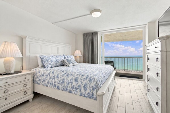 A bedroom with a bed, nightstands, a dresser, a balcony with a view of the ocean.