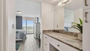 Habitación de hotel con balcón, una cama, baño con un espejo grande y una encimera con una planta.