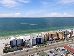 A coastal hotel with multiple buildings, a parking lot, and a beach in the background.