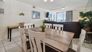 Un comedor con una mesa de madera y sillas blancas, un sofá y una planta en maceta.