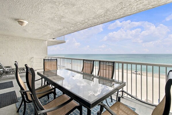 A balcony with a glass table and chairs, overlooking a beach. - Modern Comforts Meet Stunning Madeira Beach Ocean Views | 3BR at Seaview 404 | (Madeira Beach)