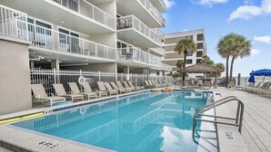 Una piscina con sillas de descanso, un indicador de profundidad de 1,8 metros y un edificio de varios pisos con balcones.