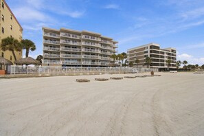 A beachfront hotel with multiple balconies, a sandy beach, and palm trees.
