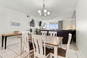 A dining area with a wooden table and white chairs, a black sofa, and a ceiling light fixture.