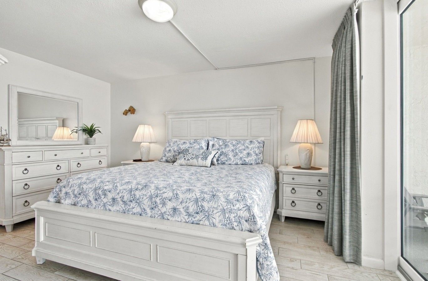 Une chambre à coucher comprenant un lit, deux tables de chevet, une commode, un miroir et un luminaire au plafond.
