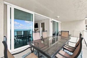 A glass-top table with chairs on a balcony with a view of the ocean. - Modern Comforts Meet Stunning Madeira Beach Ocean Views | 3BR at Seaview 404 | (Madeira Beach)