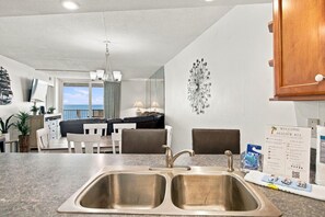 A kitchen with a double sink, a dining area with a table and chairs, and a view of the ocean.