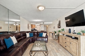 A modern living room with a leather sectional sofa, a glass coffee table, a wooden cabinet, and a flat-screen TV mounted on the wall.