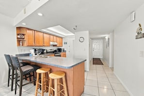 Una cocina moderna con una isla central, taburetes de bar, armarios de madera y un microondas.