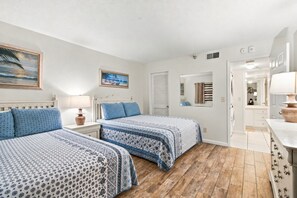 A bedroom with two beds, a nightstand with a lamp, a painting, and a mirror. - Modern Comforts Meet Stunning Madeira Beach Ocean Views | 3BR at Seaview 404 | (Madeira Beach)