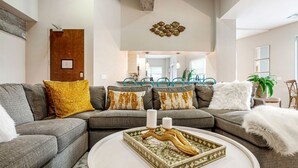 A modern living room with a sectional sofa, a coffee table with decorative items, and a dining area in the background.