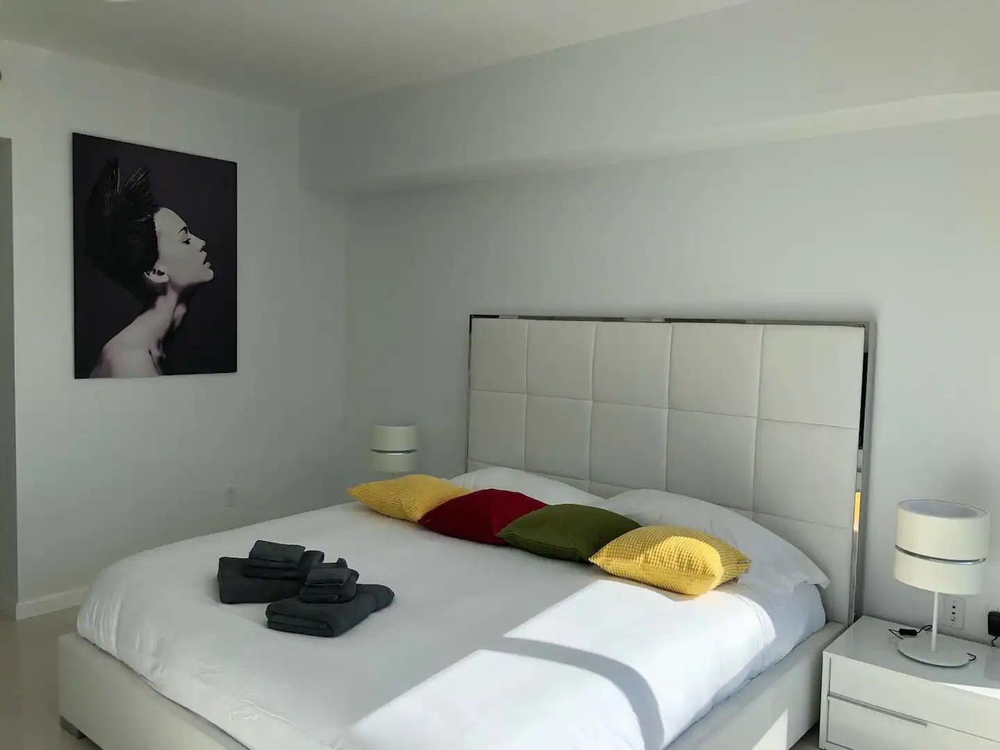 A modern hotel room with a large bed, a headboard, and a bedside table with a lamp.