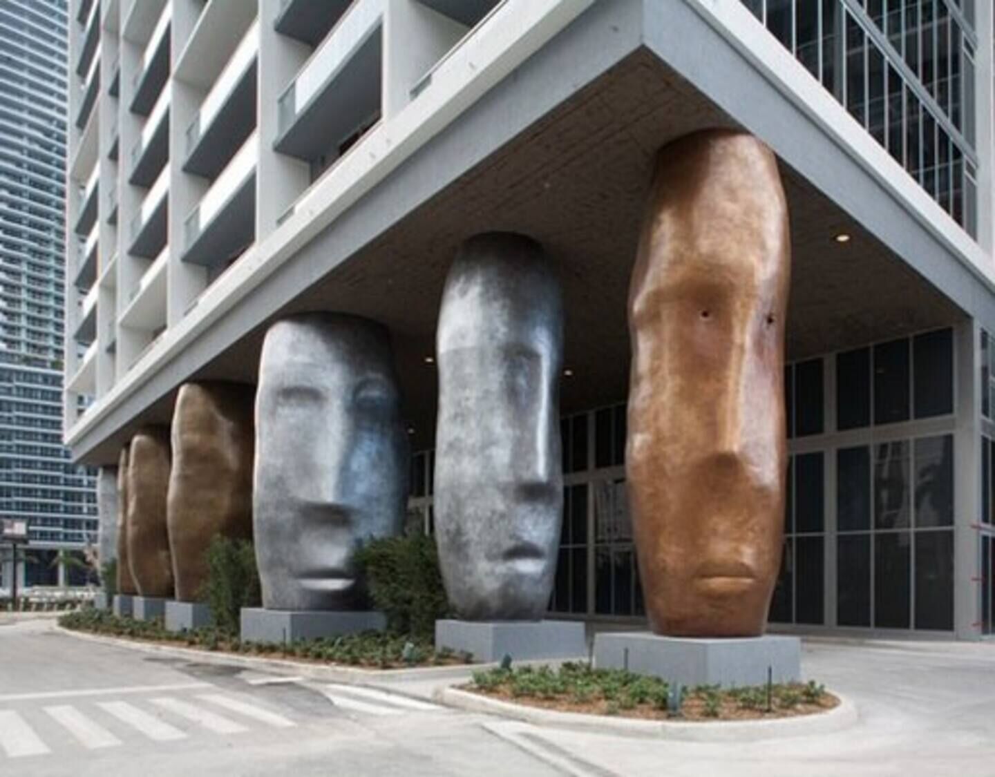 A modern building with large, abstract sculptures of human heads under a sloped roof.