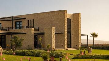 Un edificio moderno con fachada de piedra, un patio cubierto y un césped bien cuidado con flores rosas.