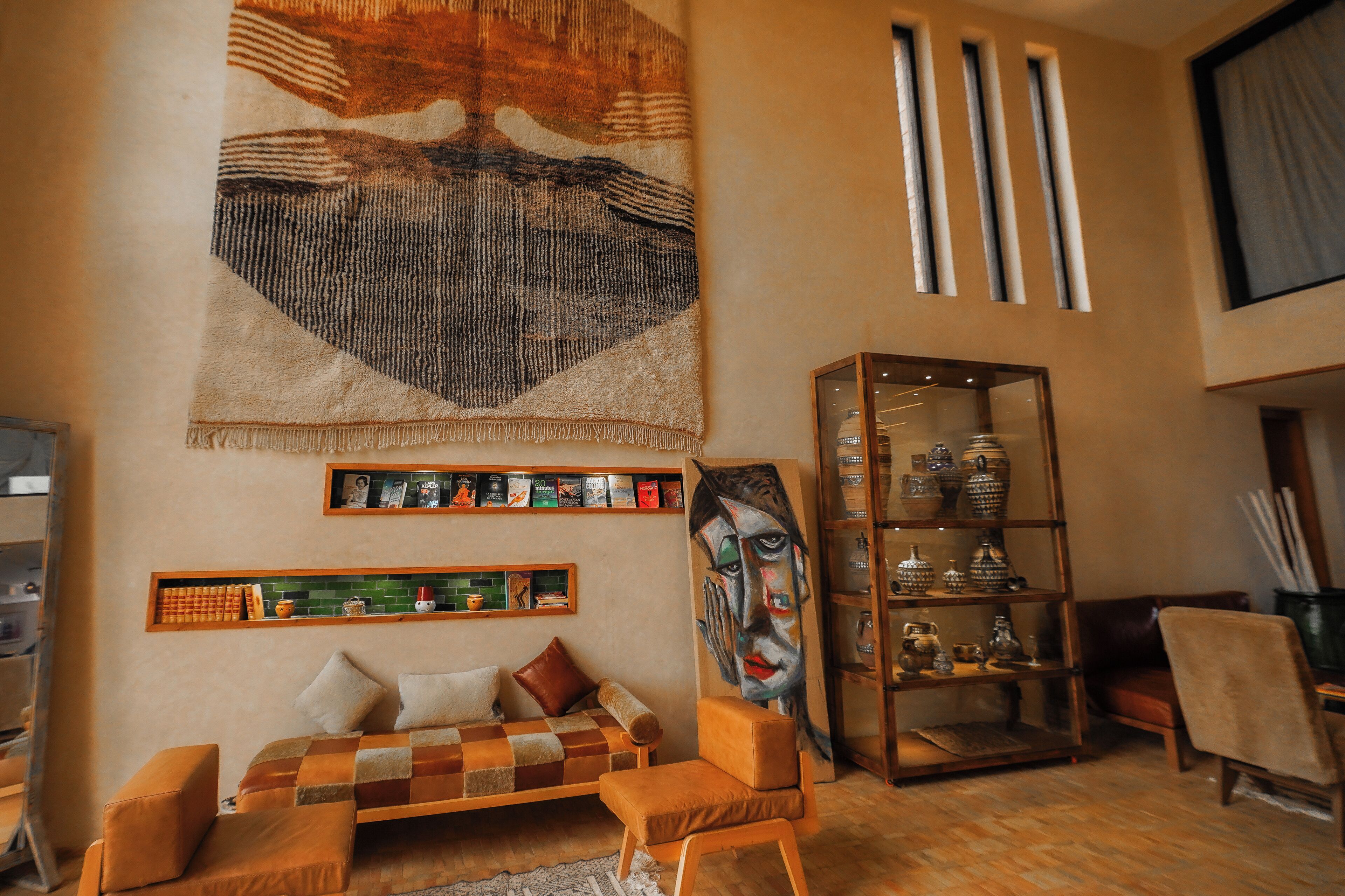 Una sala de estar acogedora con un sofá estampado de cuadros, un tapiz grande y una estantería con libros y objetos decorativos.