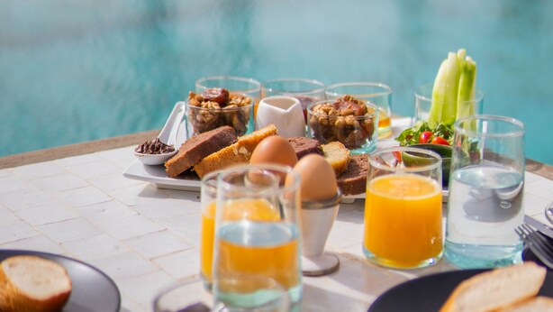 A breakfast table by a pool with various foods and drinks.