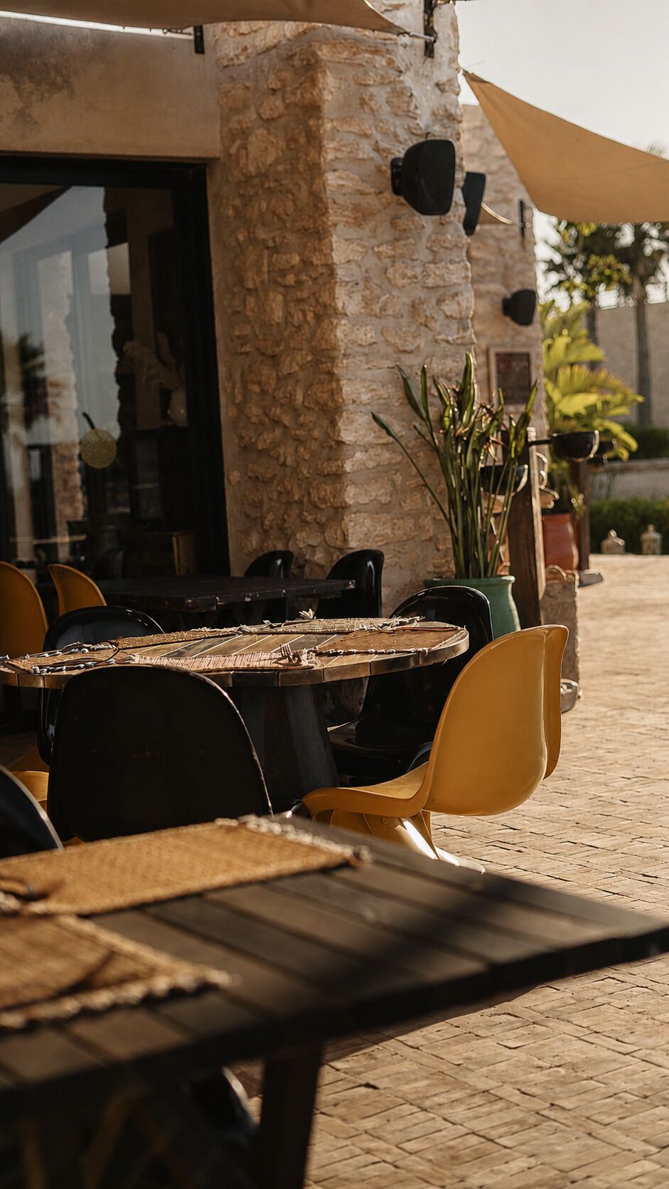 Un espacio de comedor al aire libre con pared de piedra, sillas amarillas y una mesa con un mantel tejido.