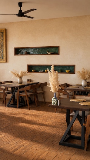 A dining area with wooden tables and chairs, a ceiling fan, and decorative wall shelves. - Baberrih Hospitality Palaces & Resorts (Moulay Bouzarqtoune)