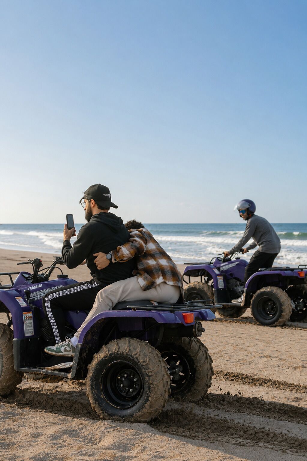 Two individuals on ATVs on a sandy beach with the ocean in the background.