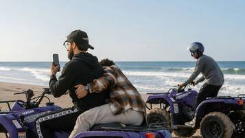 Two individuals on ATVs on a sandy beach with the ocean in the background.