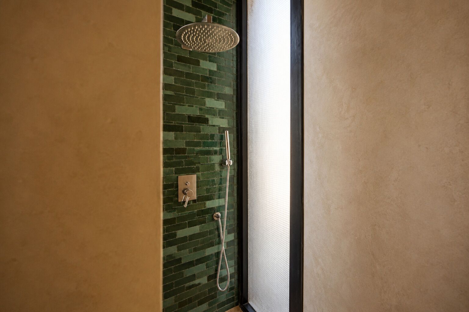 Een badkamer met een douche, een glazen deur en een betegelde muur.