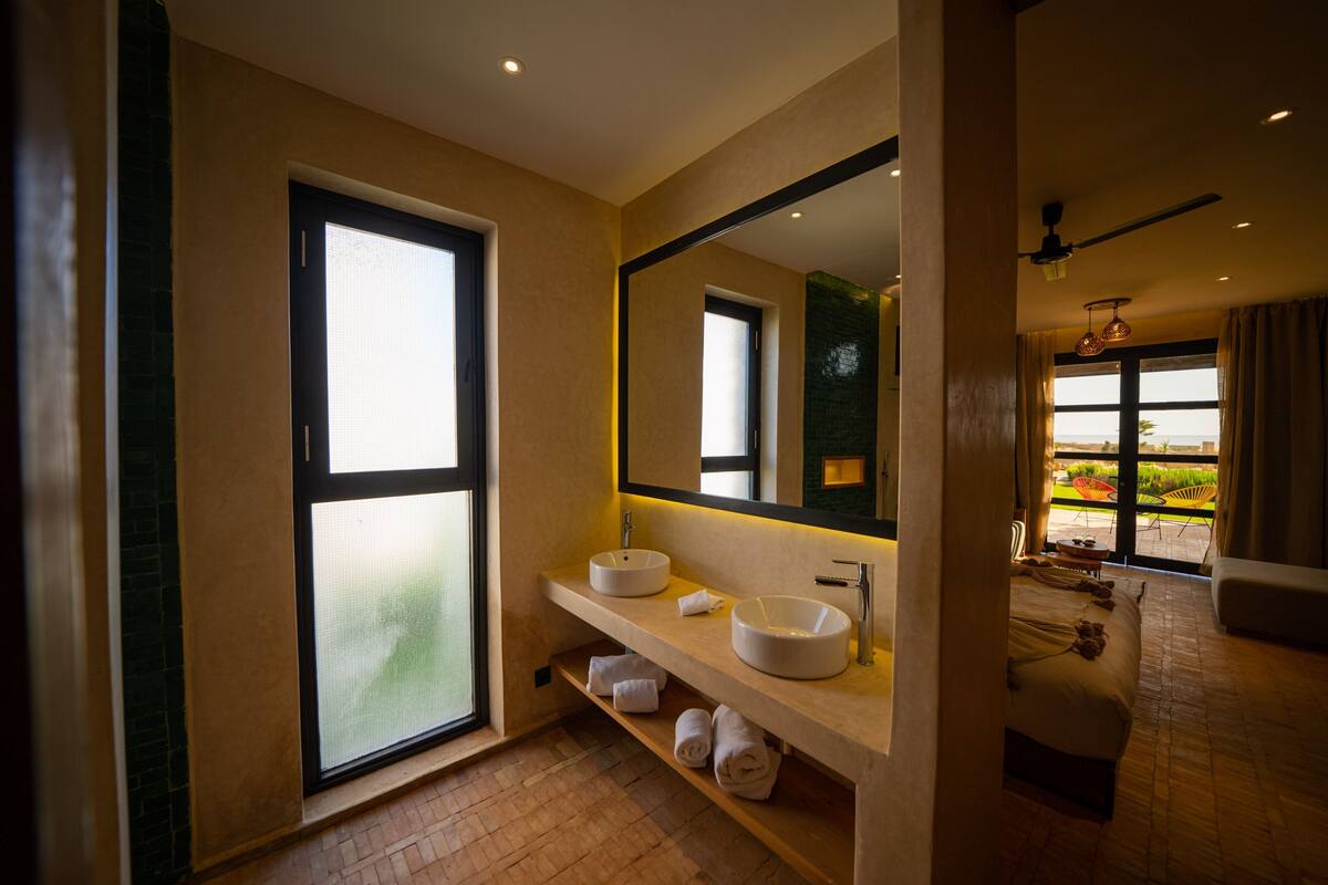 A modern bathroom with a large window, two sinks, a mirror, and a view of the outdoors.