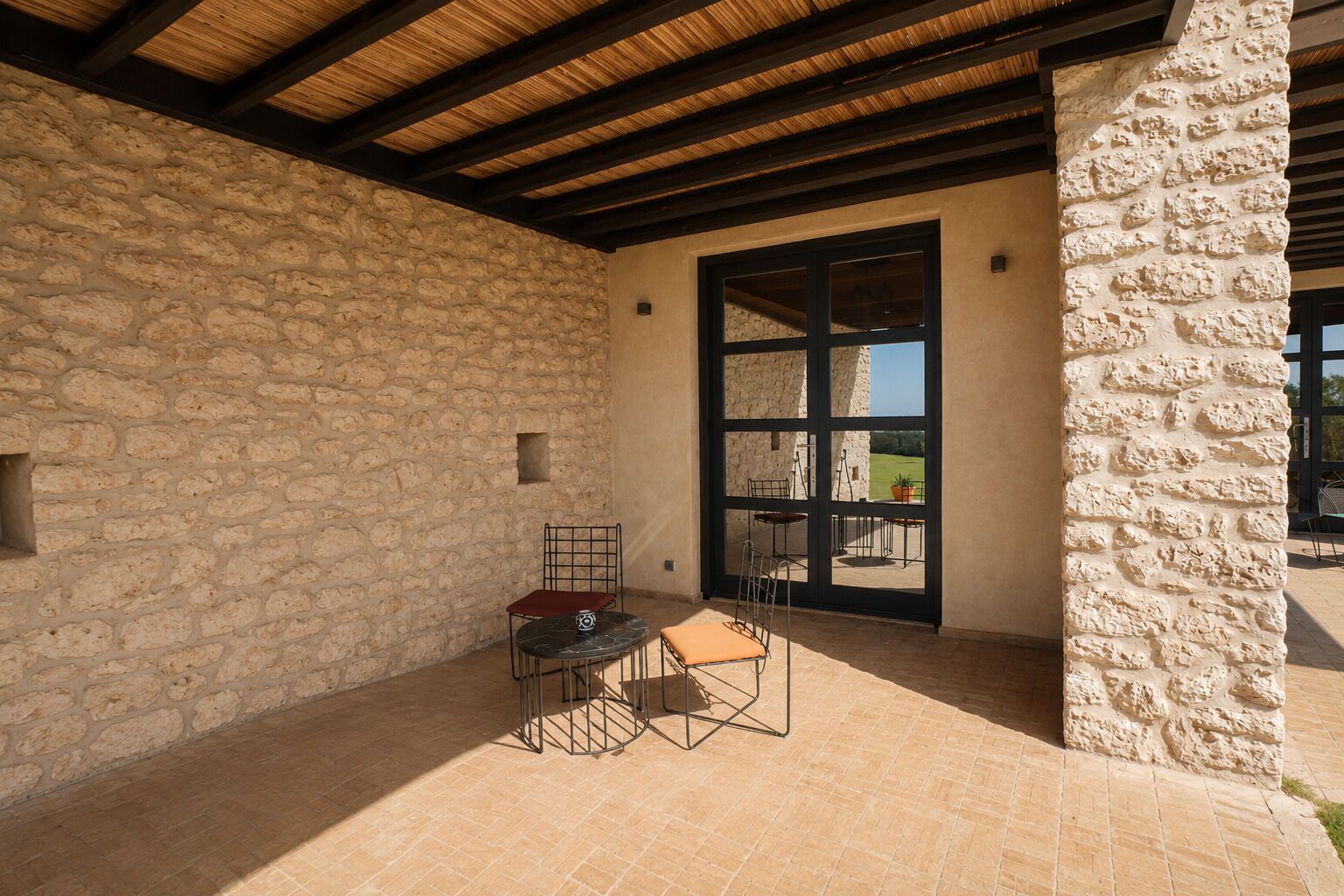 An outdoor patio with stone walls, a wooden ceiling, and a view through a glass door.