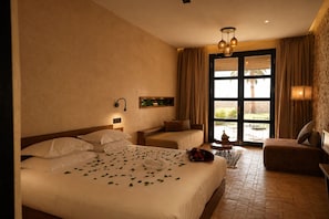 A hotel room with a large bed, a sitting area, and a view through a glass door.