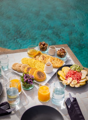 A breakfast buffet by a pool with various foods and drinks.
