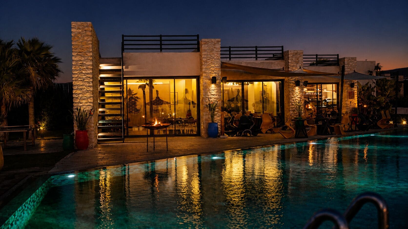 Zona junto a la piscina con un edificio moderno, asientos al aire libre y una piscina cristalina.