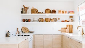 Een moderne keuken met witte kasten, houten aanrecht en planken met keukengerei en boeken.