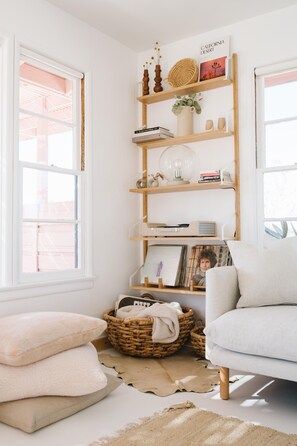 A room with a white wall, a wooden bookshelf, a white armchair, and a window with a view of a building.