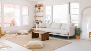 Een lichte, ruime woonkamer met een witte bank, een houten salontafel en een groot raam dat voor natuurlijk licht zorgt.