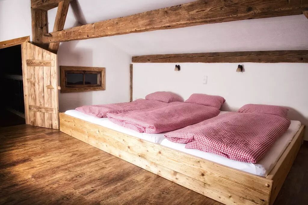 A wooden bed with checkered bedding in a room with exposed wooden beams and a small window.