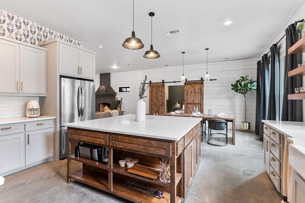 Une cuisine moderne avec des meubles blancs, un grand îlot central, des appareils en acier inoxydable et des luminaires suspendus.