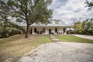 A modern house with a large tree in the front yard, a gravel driveway, and a covered porch area.