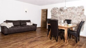 Uma sala de estar com um sofá marrom escuro, uma mesa de jantar de madeira com quatro cadeiras e uma parede de pedra.