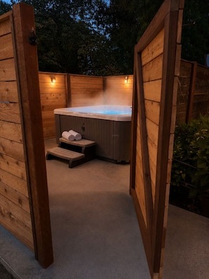 A wooden hot tub with steps and towels, surrounded by wooden walls and a concrete floor.