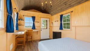 A cozy room with a bed, a desk, and a chair. There are windows with curtains, a door, and a chandelier. - Quiet Glamping Barn on a Working Farm with Fire Pit and Open Views (Lynden)