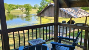 Una terraza de madera con sillas Adirondack y una mesa, con vistas a un lago y un edificio.