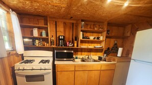 Una cocina compacta con gabinetes de madera, estufa a gas, microondas y refrigerador.