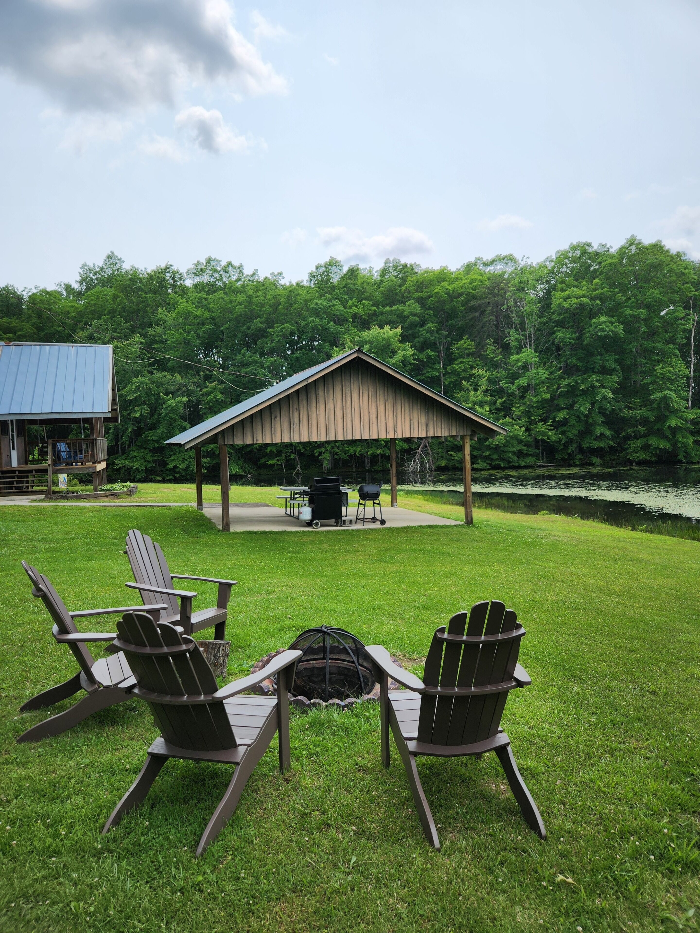 A covered outdoor seating area with Adirondack chairs, a grill, and a table set up for dining.